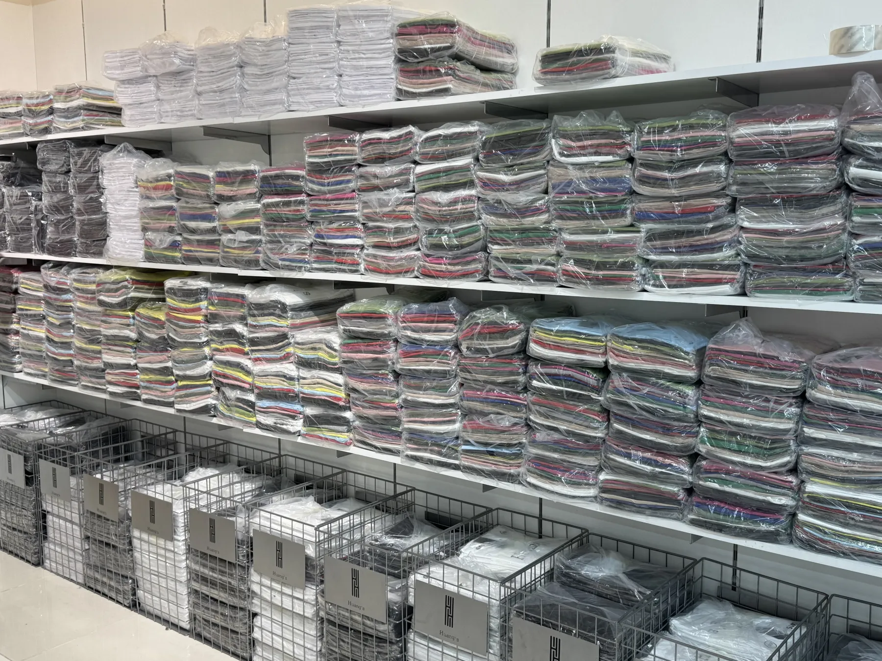 HUANG'S stockroom — shelves of folded seasonal tops and HUANG'S branded storage bins
